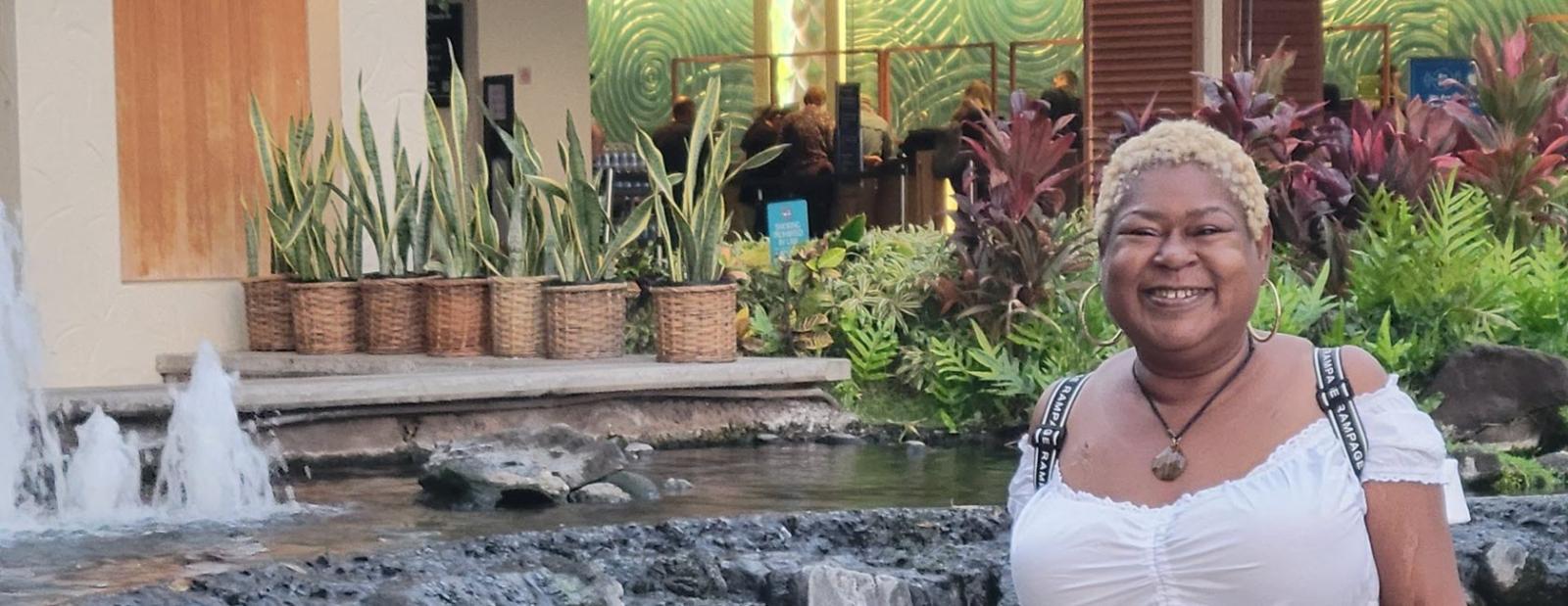  A woman stands before a fountain with a waterfall, surrounded by lush topical plants in the background